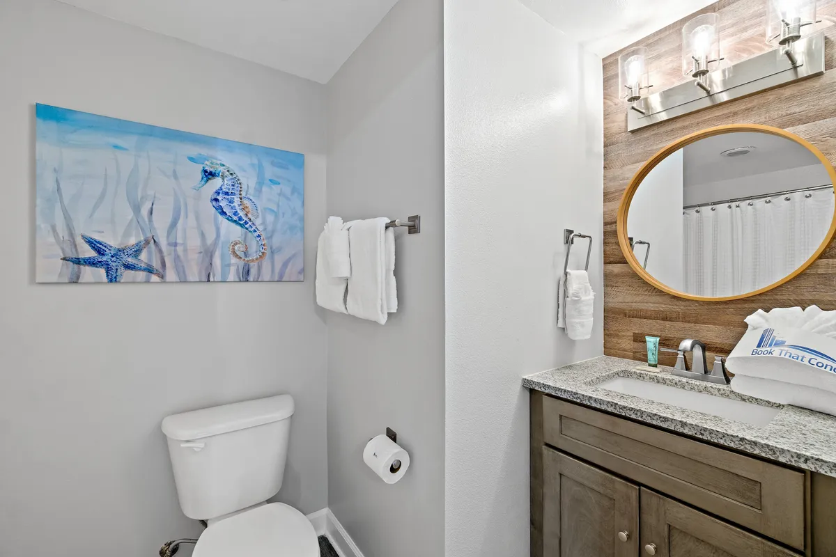 A modern bathroom featuring granite countertops, a round mirror, and seahorse artwork that adds a coastal touch. The space is bright and clean, designed for comfort and convenience.