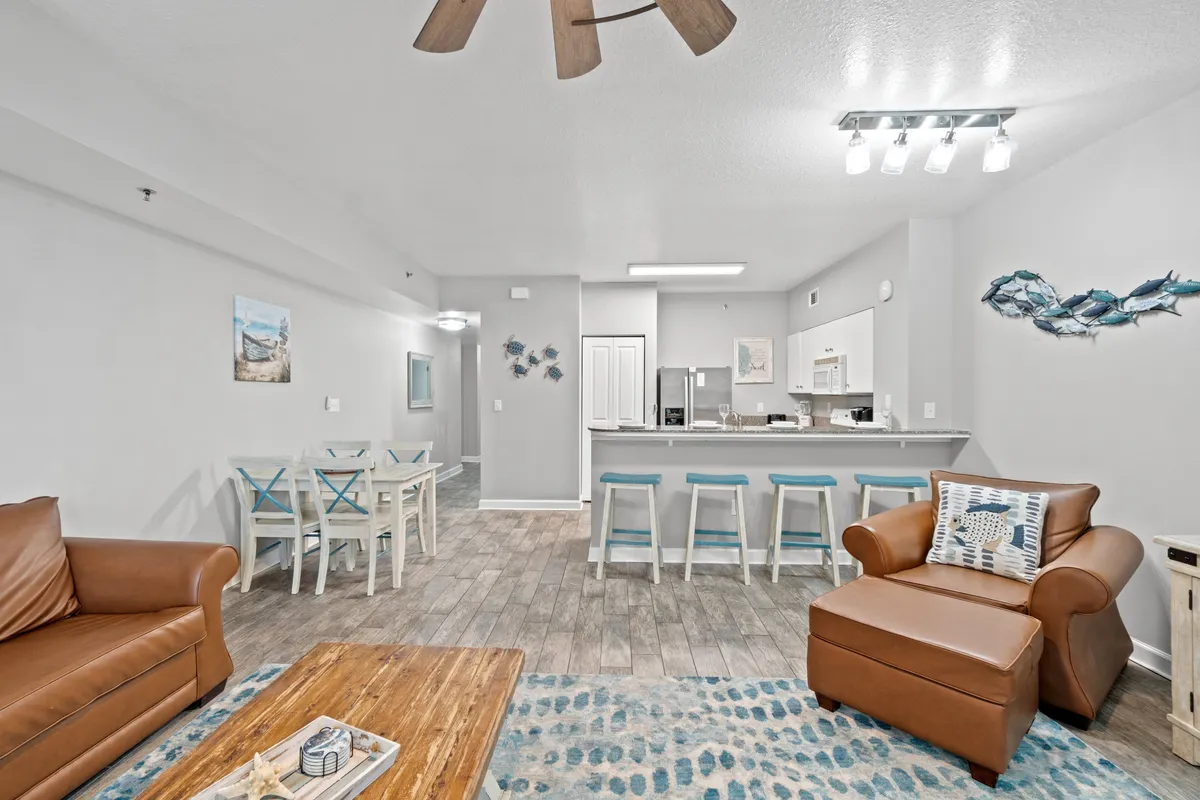 A cozy and inviting living area featuring a leather sofa, a wooden coffee table, a dining table with chairs, kitchen bar stools, and decorative fish artwork on the wall. The space feels perfect for group gatherings, socializing, and enjoying shared meals, with a warm, welcoming ambiance.