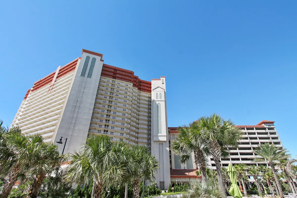 The striking high-rise Shores of Panama resort, surrounded by lush palm trees and tropical landscaping, commands a vibrant beachfront presence. The multi-level parking structure is visible, offering a glimpse of the effortless access promised to guests.