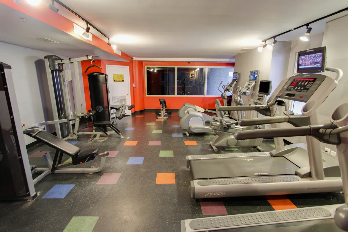 A modern health and fitness center features treadmills, a weight bench, and colorful flooring, with a large window offering a glimpse of the outdoors. The space is bright and motivating, designed for guests to start their day with wellness in mind.