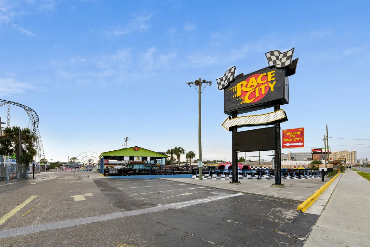 The lively scene at Race City features the iconic sign, a visible go-kart track, and amusement rides in the background. Palm trees and sunny skies amplify the energetic, fun atmosphere suitable for both families and couples.