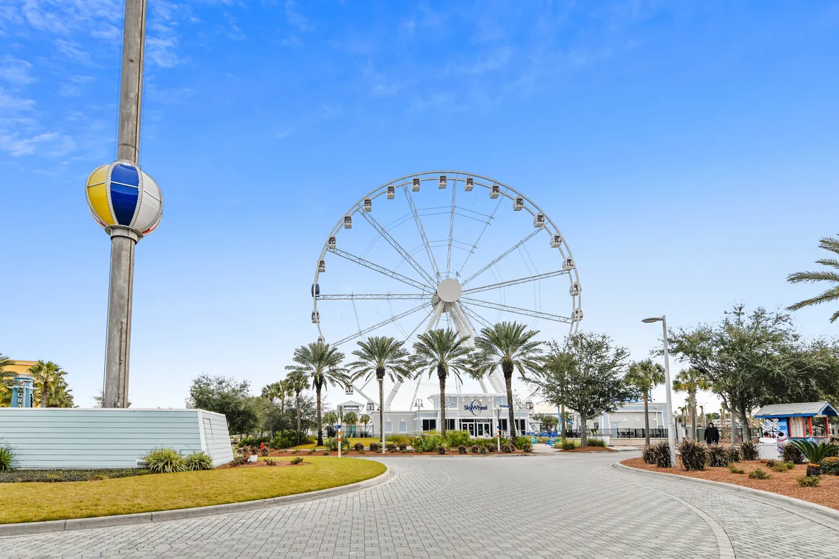 This image features the entrance to Shipwreck Island Water Park, with a large Ferris wheel, palm trees, and a colorful beach-ball sculpture. The entrance building sets a playful, adventurous tone, and the scene is buzzing with energy and anticipation for water-based activities.